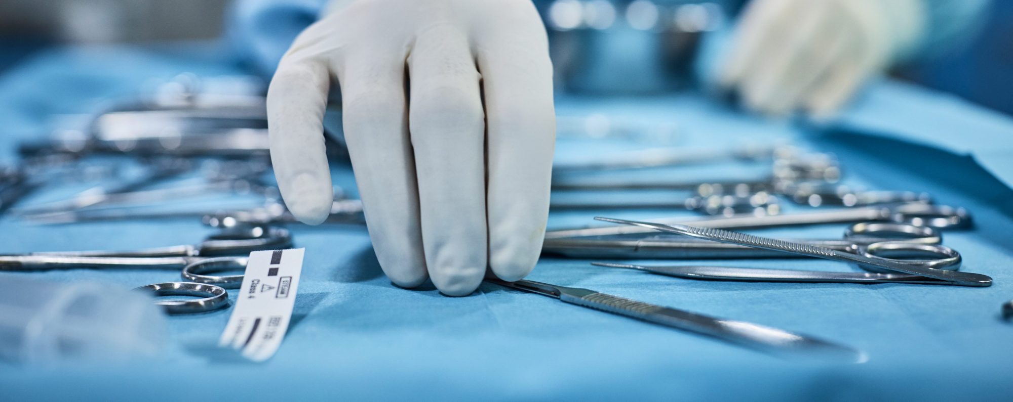 Closeup of surgeon's hand picking up surgical tools from tray.